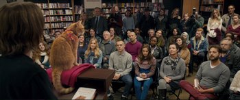 Movie still from “A Street Cat Named Bob” (2016), directed by Roger Spottiswoode – A group of people sitting in front of an orange cat; Wide shot, High angle