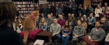 Movie still from “A Street Cat Named Bob” (2016), directed by Roger Spottiswoode – A group of people sitting in front of an orange cat; Wide shot, High angle