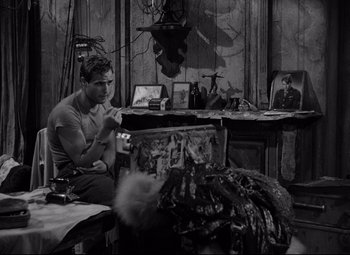 Movie still from “A Streetcar Named Desire” (1951), directed by Elia Kazan – A black and white photo of a man sitting in front of a fireplace; Medium shot, Over the shoulder angle