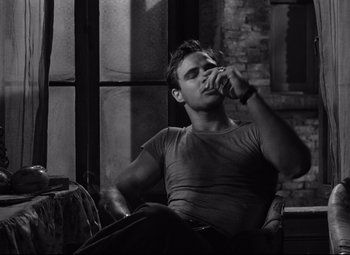 Movie still from “A Streetcar Named Desire” (1951), directed by Elia Kazan – A man sitting in a chair drinking a beverage; Medium shot, Over the shoulder angle