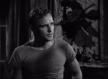 Movie still from “A Streetcar Named Desire” (1951), directed by Elia Kazan – Black and white photograph of a man in a t - shirt looking to his left; Medium shot, Over the shoulder angle