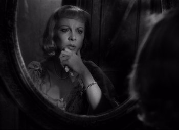 A black and white photo of a woman looking at herself in a mirror