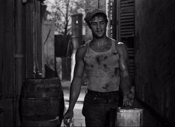 Movie still from “A Streetcar Named Desire” (1951), directed by Elia Kazan – A man in a tank top walking down a street; Medium shot, Over the shoulder angle