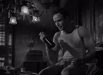 Movie still from “A Streetcar Named Desire” (1951), directed by Elia Kazan – A man holding a bottle of wine in his hand; Medium shot, Low angle