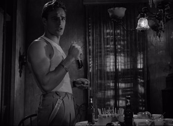 Movie still from “A Streetcar Named Desire” (1951), directed by Elia Kazan – A man holding a beer in his hand and standing in front of a table; Medium shot, Low angle