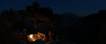 A person sitting on top of a rock near a fire
