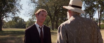 Movie still from “A Time to Kill” (1996), directed by Joel Schumacher – A man wearing a suit and tie standing next to a man wearing a hat; Medium shot, Over the shoulder angle