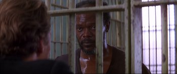 Movie still from “A Time to Kill” (1996), directed by Joel Schumacher – A man in brown shirt behind bars looking at the camera; Close Up shot, Over the shoulder angle