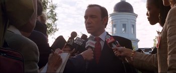 Movie still from “A Time to Kill” (1996), directed by Joel Schumacher – A man in a suit and red tie is being interviewed by reporters; Close Up shot, Low angle