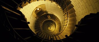 Movie still from “A Very Long Engagement” (2004), directed by Jean-Pierre Jeunet – Looking down at a spiral staircase in a building; Extreme Wide shot, Overhead angle