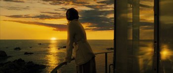 Movie still from “A Very Long Engagement” (2004), directed by Jean-Pierre Jeunet – A woman standing on a balcony looking out at the ocean; Medium shot, Low angle