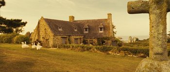 Movie still from “A Very Long Engagement” (2004), directed by Jean-Pierre Jeunet – An old stone house in a field with a sky background; Extreme Wide shot, High angle