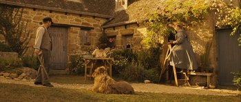Movie still from “A Very Long Engagement” (2004), directed by Jean-Pierre Jeunet – A dog sitting in the grass next to a table; Wide shot, High angle