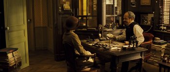 Movie still from “A Very Long Engagement” (2004), directed by Jean-Pierre Jeunet – A person sitting at a desk in front of a window; Wide shot, High angle
