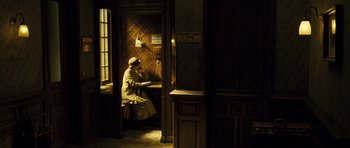 Movie still from “A Very Long Engagement” (2004), directed by Jean-Pierre Jeunet – A man sitting at a desk in a room; Wide shot, High angle