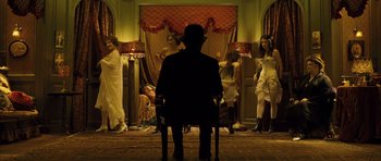 Movie still from “A Very Long Engagement” (2004), directed by Jean-Pierre Jeunet – A man sitting in a chair in front of a group of women; Wide shot, High angle