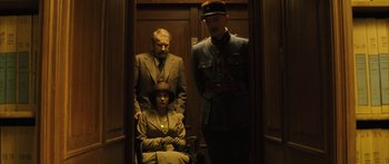 Movie still from “A Very Long Engagement” (2004), directed by Jean-Pierre Jeunet – A man and a woman standing in an elevator with a man in a uniform; Medium shot, Low angle