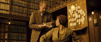 Movie still from “A Very Long Engagement” (2004), directed by Jean-Pierre Jeunet – An older man and a young woman in a library; Medium shot, Low angle