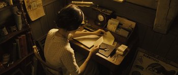 Movie still from “A Very Long Engagement” (2004), directed by Jean-Pierre Jeunet – A woman sitting at a desk working on papers; Medium shot, High angle