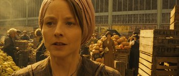 Movie still from “A Very Long Engagement” (2004), directed by Jean-Pierre Jeunet – A woman with a head scarf standing in front of an outdoor market; Close Up shot, Over the shoulder angle