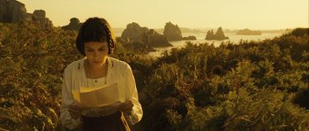 Movie still from “A Very Long Engagement” (2004), directed by Jean-Pierre Jeunet – A woman standing in a field looking at a piece of paper; Medium shot, High angle
