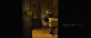 Movie still from “A Very Long Engagement” (2004), directed by Jean-Pierre Jeunet – A woman sitting at a table writing on a piece of paper; Wide shot, High angle