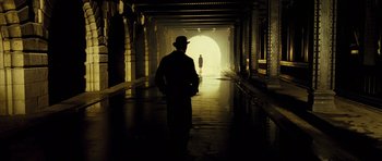 Movie still from “A Very Long Engagement” (2004), directed by Jean-Pierre Jeunet – A man wearing a hat walking down a dark hallway; Wide shot, Over the shoulder angle