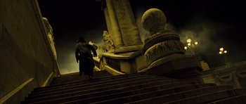 Movie still from “A Very Long Engagement” (2004), directed by Jean-Pierre Jeunet – A person walking up some stairs near a pillar; Wide shot, Low angle