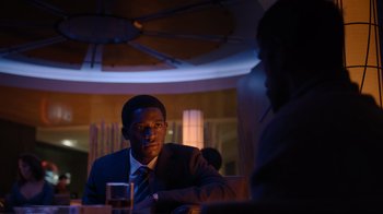 Movie still from “Snowfall” (2017), directed by Hiro Murai – A man sitting at a table in front of a glass of water; Medium shot, Over the shoulder angle