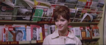Movie still from “A Woman Is a Woman” (1961), directed by Jean-Luc Godard – A woman standing in front of a bunch of books; Close Up shot, Over the shoulder angle