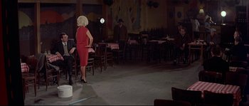 Movie still from “A Woman Is a Woman” (1961), directed by Jean-Luc Godard – A woman in a red dress standing in front of a man in a black suit; Wide shot, High angle