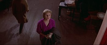 Movie still from “A Woman Is a Woman” (1961), directed by Jean-Luc Godard – An older woman in a purple shirt is holding a box; Medium shot, High angle