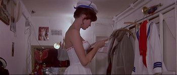 Movie still from “A Woman Is a Woman” (1961), directed by Jean-Luc Godard – A woman in a white dress and a sailor's hat is looking at a piece of paper; Medium shot, Low angle