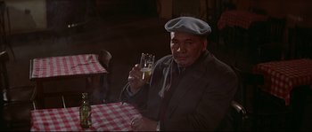 Movie still from “A Woman Is a Woman” (1961), directed by Jean-Luc Godard – An older man sitting at a table with a glass of beer in front of him; Medium shot, High angle