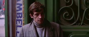 Movie still from “A Woman Is a Woman” (1961), directed by Jean-Luc Godard – A man in a gray coat and a gray sweater; Close Up shot, Low angle