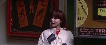 Movie still from “A Woman Is a Woman” (1961), directed by Jean-Luc Godard – A young woman with long brown hair wearing a white jacket; Close Up shot, Over the shoulder angle