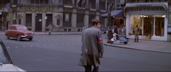 Movie still from “A Woman Is a Woman” (1961), directed by Jean-Luc Godard – A man walking down the street wearing a coat; Medium shot, High angle