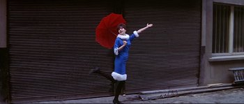Movie still from “A Woman Is a Woman” (1961), directed by Jean-Luc Godard – A woman in a blue dress holding a red umbrella; Wide shot, Low angle