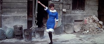 Movie still from “A Woman Is a Woman” (1961), directed by Jean-Luc Godard – A woman in a blue dress and a white fur trimmed hat; Medium shot, Low angle