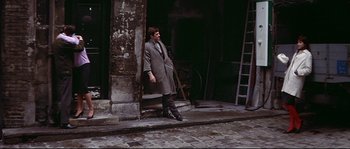 Movie still from “A Woman Is a Woman” (1961), directed by Jean-Luc Godard – A man standing on the side of the street; Wide shot, High angle
