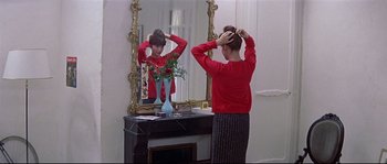 Movie still from “A Woman Is a Woman” (1961), directed by Jean-Luc Godard – A woman standing in front of a mirror and holding her hair; Medium shot, Over the shoulder angle