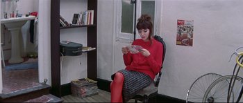 Movie still from “A Woman Is a Woman” (1961), directed by Jean-Luc Godard – A woman sitting in a chair looking at a book; Medium shot, High angle