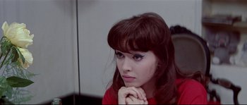 Movie still from “A Woman Is a Woman” (1961), directed by Jean-Luc Godard – A young woman with blue eye shadow is holding her chin; Close Up shot, High angle