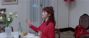 Movie still from “A Woman Is a Woman” (1961), directed by Jean-Luc Godard – A woman in a red shirt sitting at a table; Medium shot, Over the shoulder angle