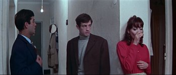 Movie still from “A Woman Is a Woman” (1961), directed by Jean-Luc Godard – A man in a brown jacket standing next to a woman in a red dress; Medium shot, Low angle