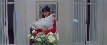 Movie still from “A Woman Is a Woman” (1961), directed by Jean-Luc Godard – A woman holding a pillow in a room with flowers; Medium shot, High angle
