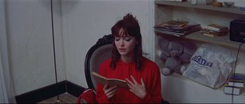 Movie still from “A Woman Is a Woman” (1961), directed by Jean-Luc Godard – A woman sitting in a chair reading a book; Medium shot, Over the shoulder angle
