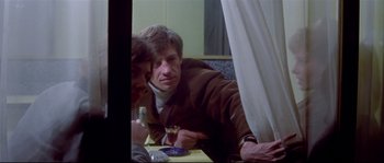 Movie still from “A Woman Is a Woman” (1961), directed by Jean-Luc Godard – A man sitting at a table with a glass of wine; Medium shot, Over the shoulder angle