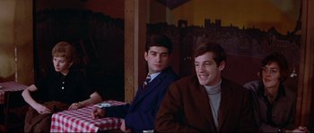 Movie still from “A Woman Is a Woman” (1961), directed by Jean-Luc Godard – Two young men sitting at a table in a restaurant; Medium shot, Over the shoulder angle