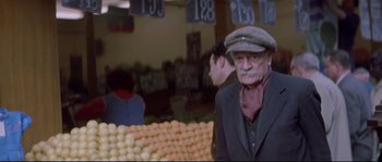 Movie still from “A Woman Is a Woman” (1961), directed by Jean-Luc Godard – An old man wearing a hat standing in front of fruit; Medium shot, Over the shoulder angle
